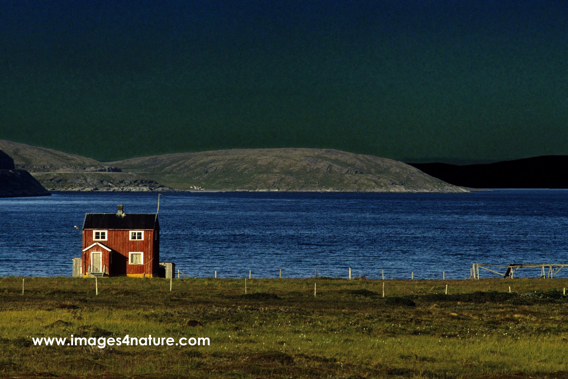 A lonely red painted wooden house on the shores of a fjord