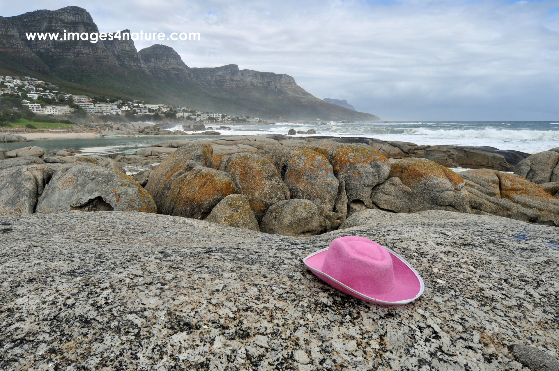 Pink hat on large boulder against sea and mountain range