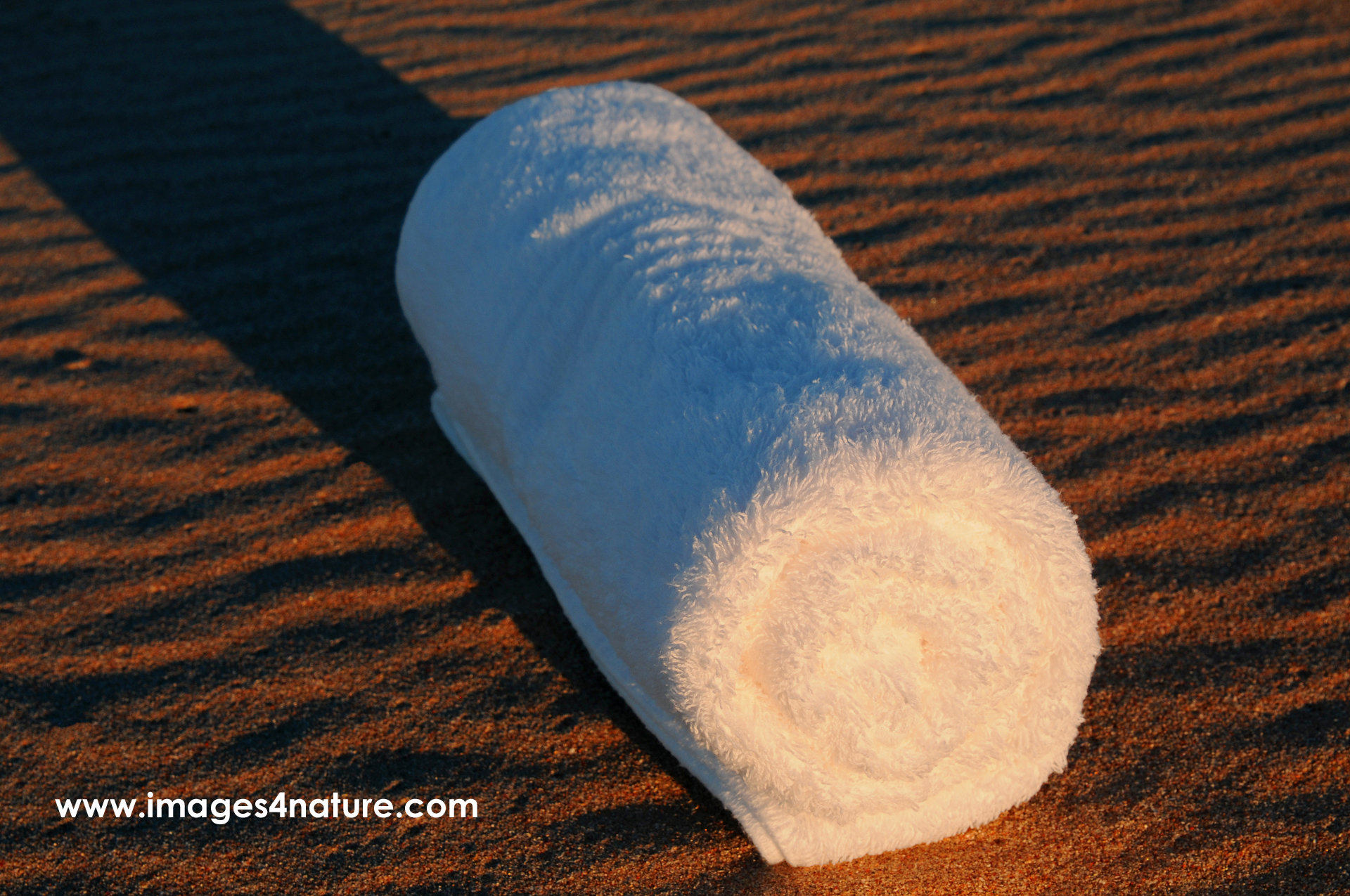 Folded white towel lying on rippled red sand at sunset