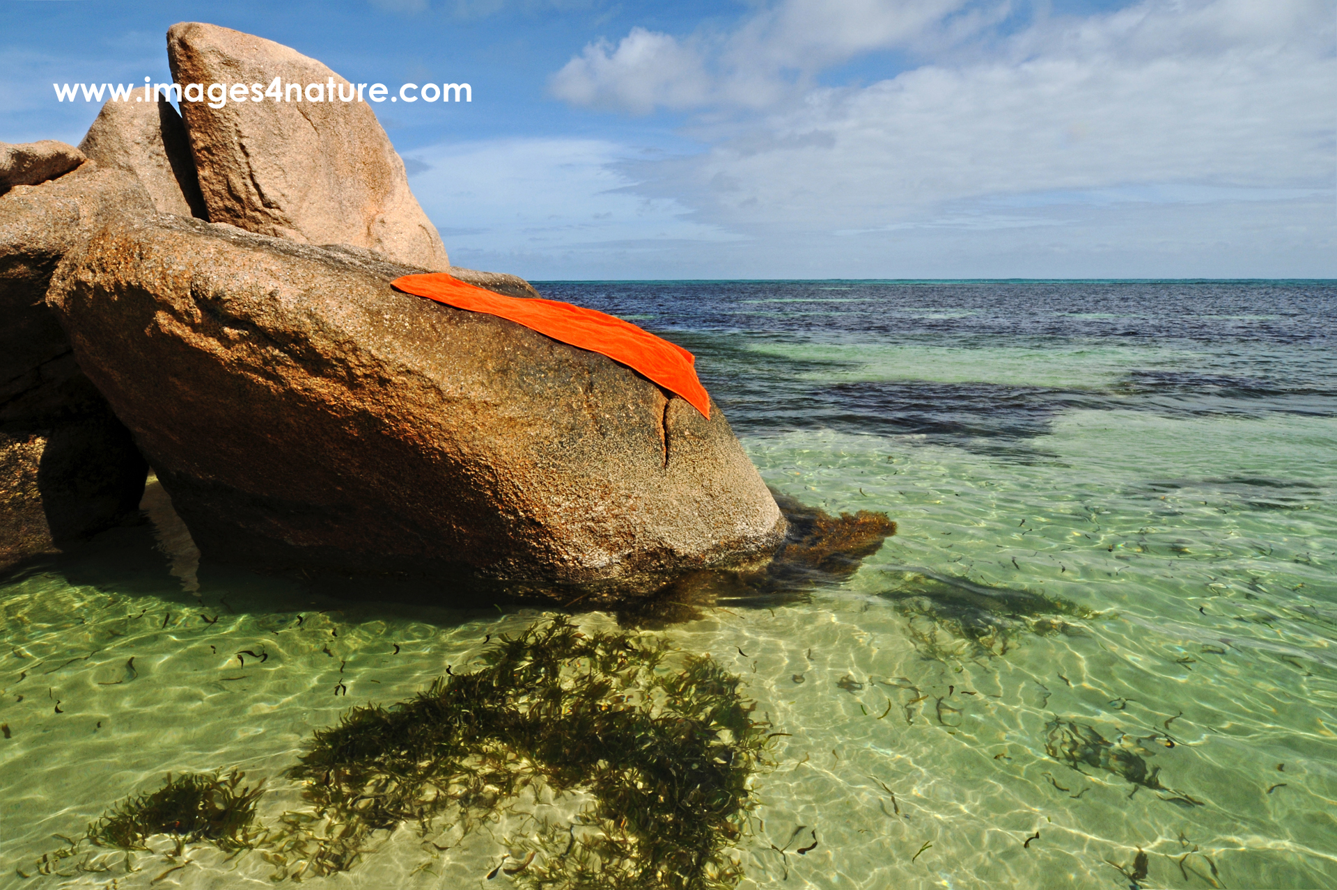 One orange beach towel lying on granite rock in tropical waters