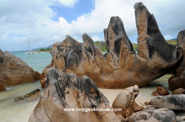 Teeth-shaped granite rocks on a tropical beach with catamaran