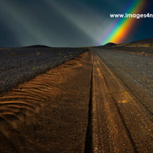 An iceland gravel road with colorful rainbow and dark sky