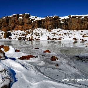 Stream flowing through Lesotho winter mountain landscape covered with snow and ice