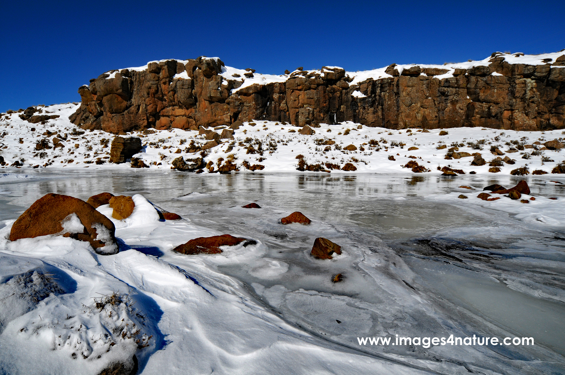 Stream flowing through Lesotho winter mountain landscape covered with snow and ice