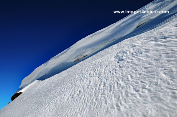 Low angle view of a steep wall of snow against the dark blue cloudless Lesotho winter sky