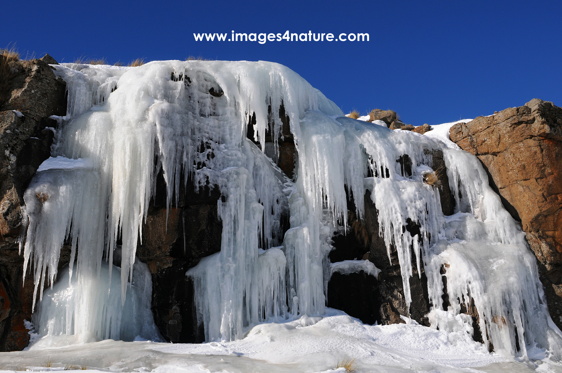 Red rocks in Lesotho winter landscape, covered with a frozen waterfall of icicles