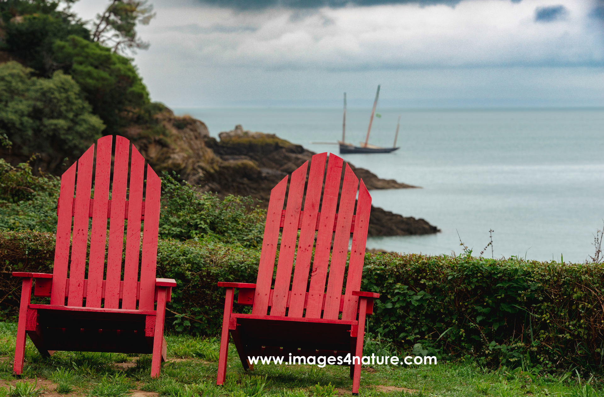 For many, sailing boats maintain a high attraction, and are associated with freedom, adventure and beautiful trips around the world  For this reason, I was happy to get one into this image of the two red deckchairs  I found them in October 2022 in France  Brittany is worth visiting at any season throughout the year  The coastline is quite diverse with breathtaking views overlooking the sea  A beautfiul hiking trail leads from Basse Cancale to Pointe du Grouin  After every corner, interesting surprises and new motives await the curious photographer   France, Basse Cancale, October 2022   Image ID 202210 FR 22