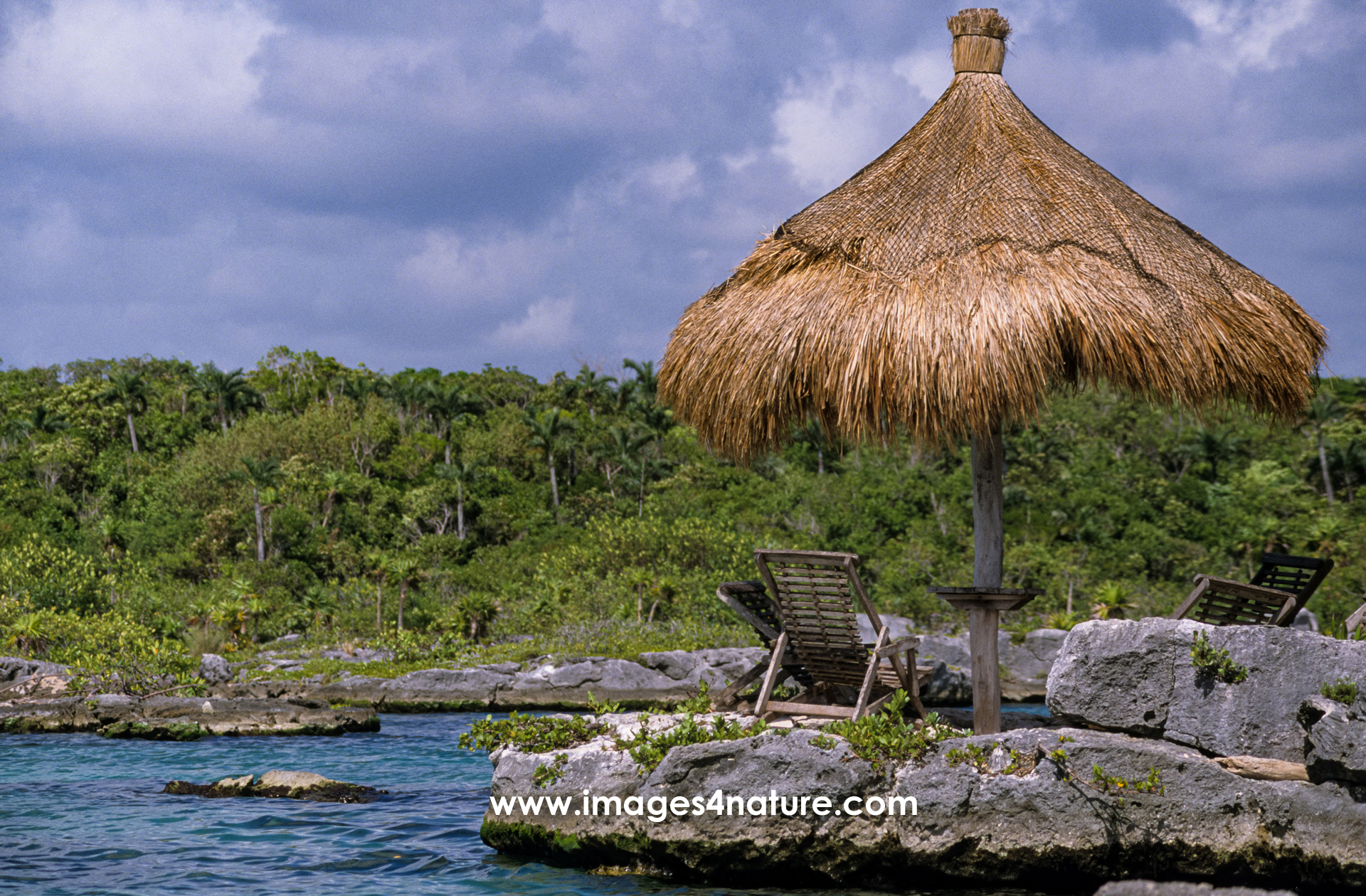 Sunshade and wooden chairs located on rocks of a tropical bay