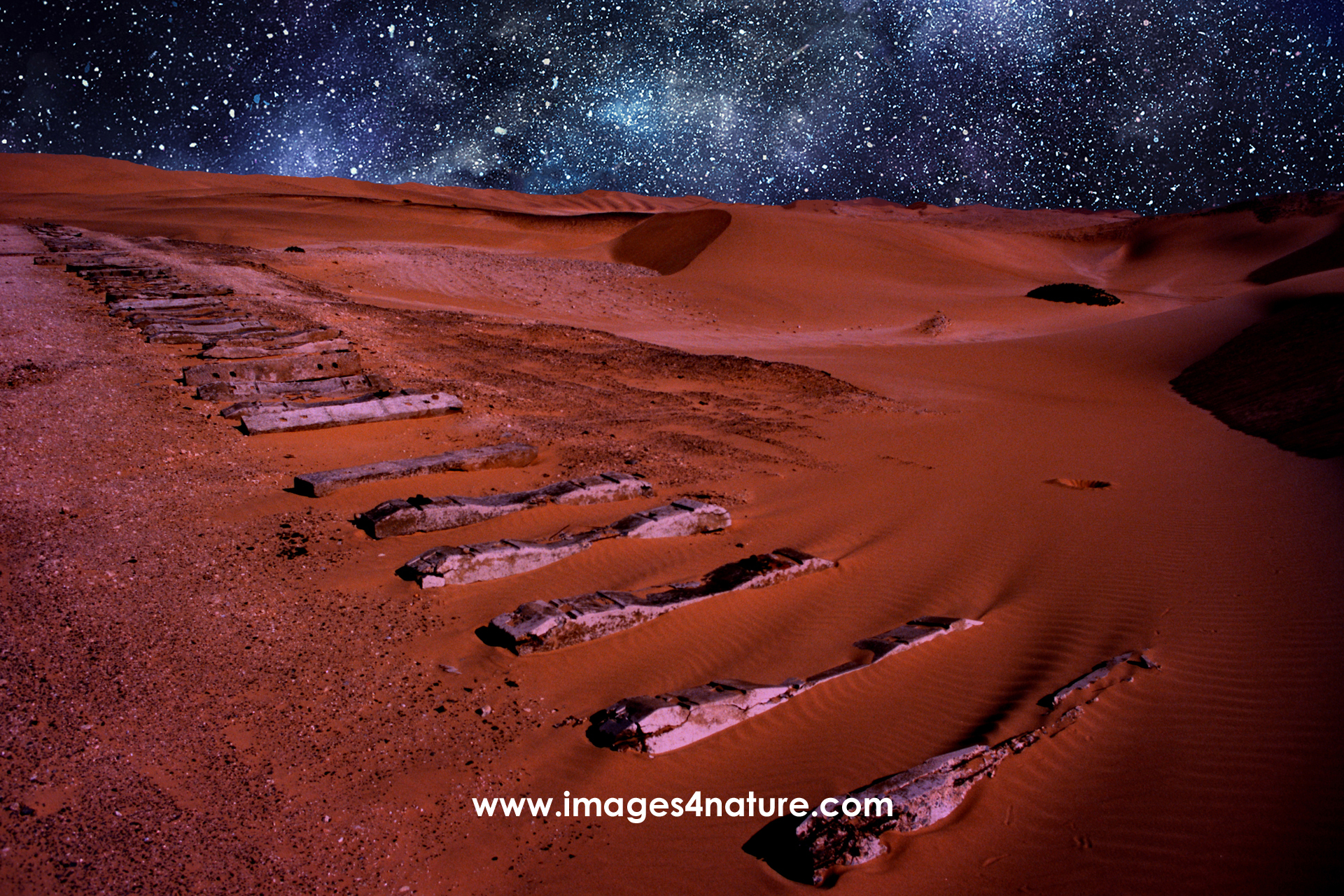 Wooden railway sleepers in red sand dunes against night sky