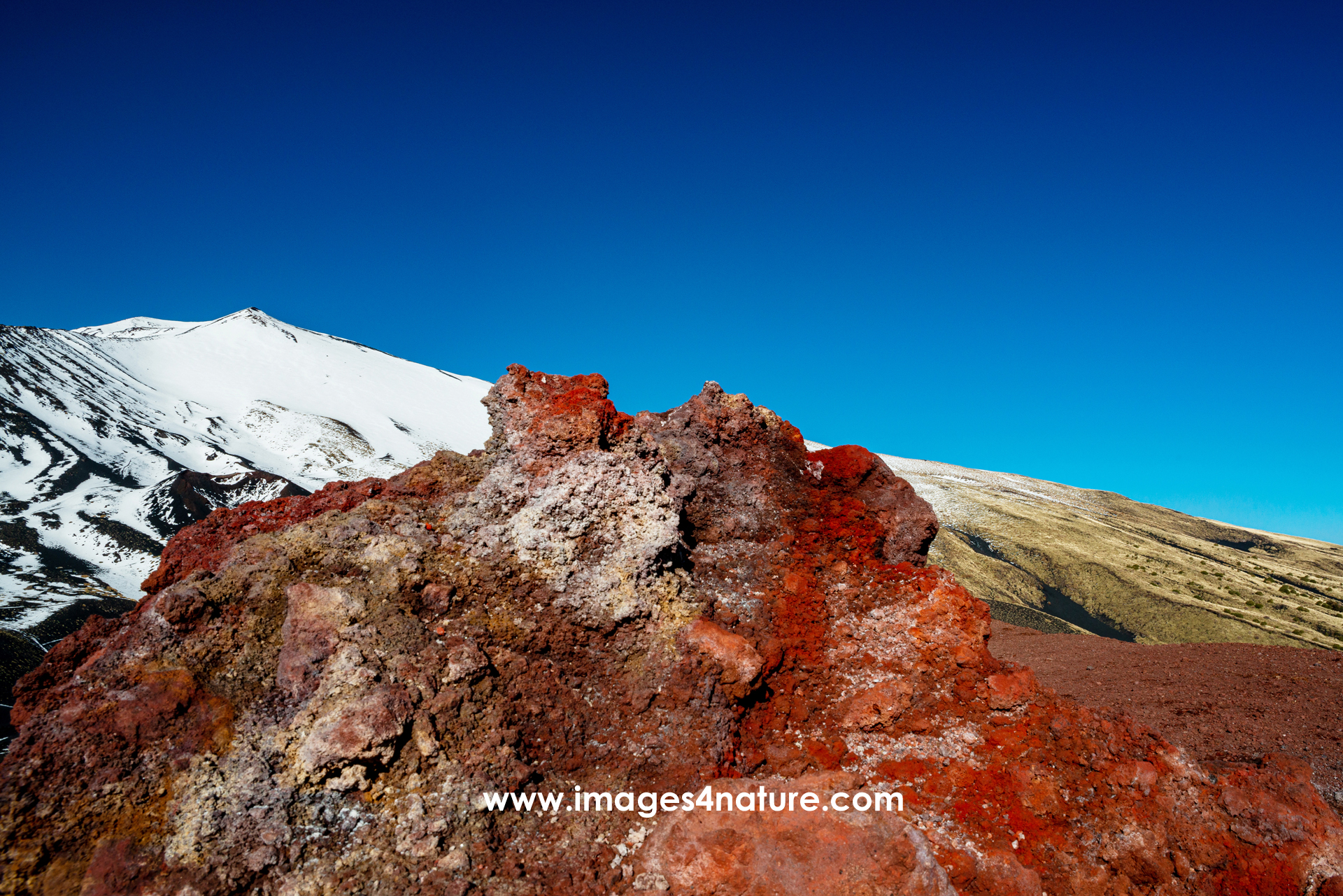Intense red colored rock against snow covered Etna volcano peak