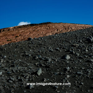 Low angle view of black and red lava fields against sky with single cloud