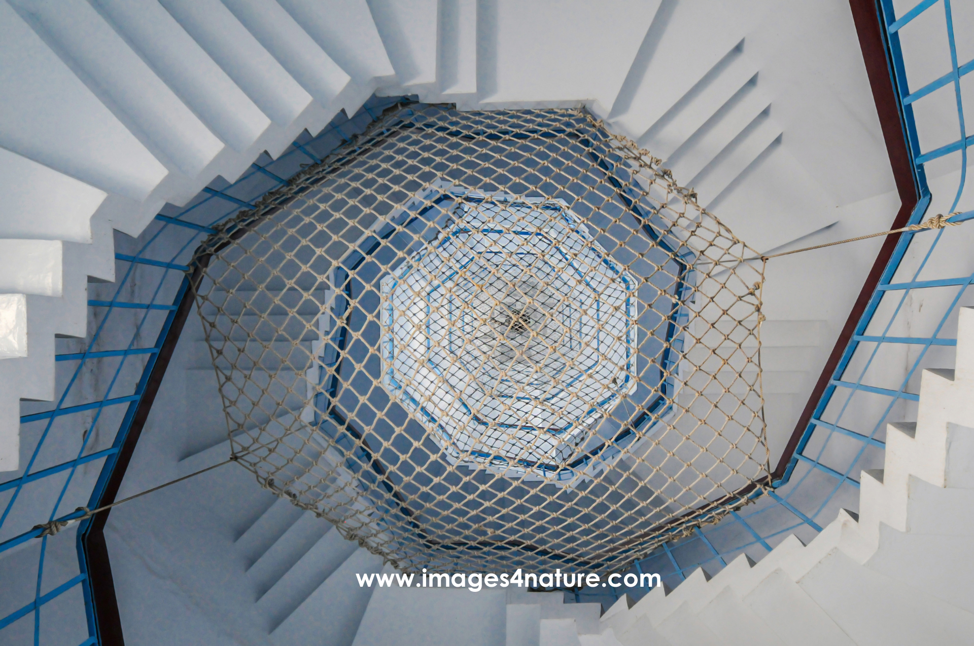 Looking down a hexagonal blue white staircase with safety net