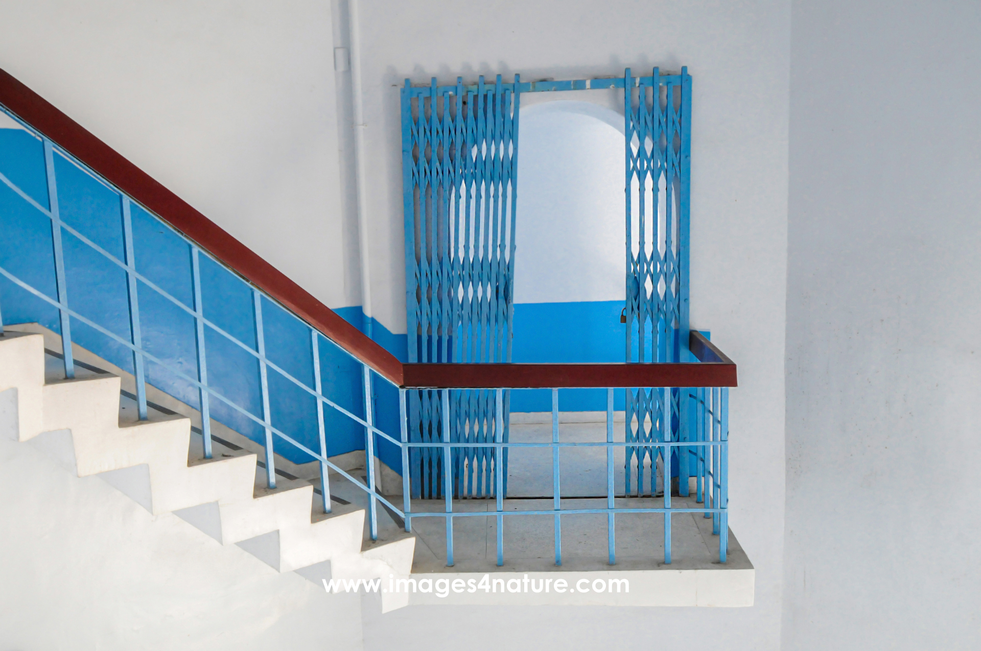 Half-open blue metal door and white staircase with wooden railing