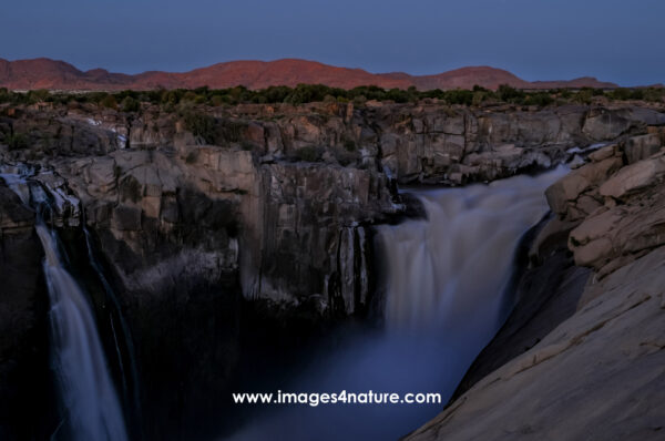 Impressive waterfall flowing down a rock valley during blue hour