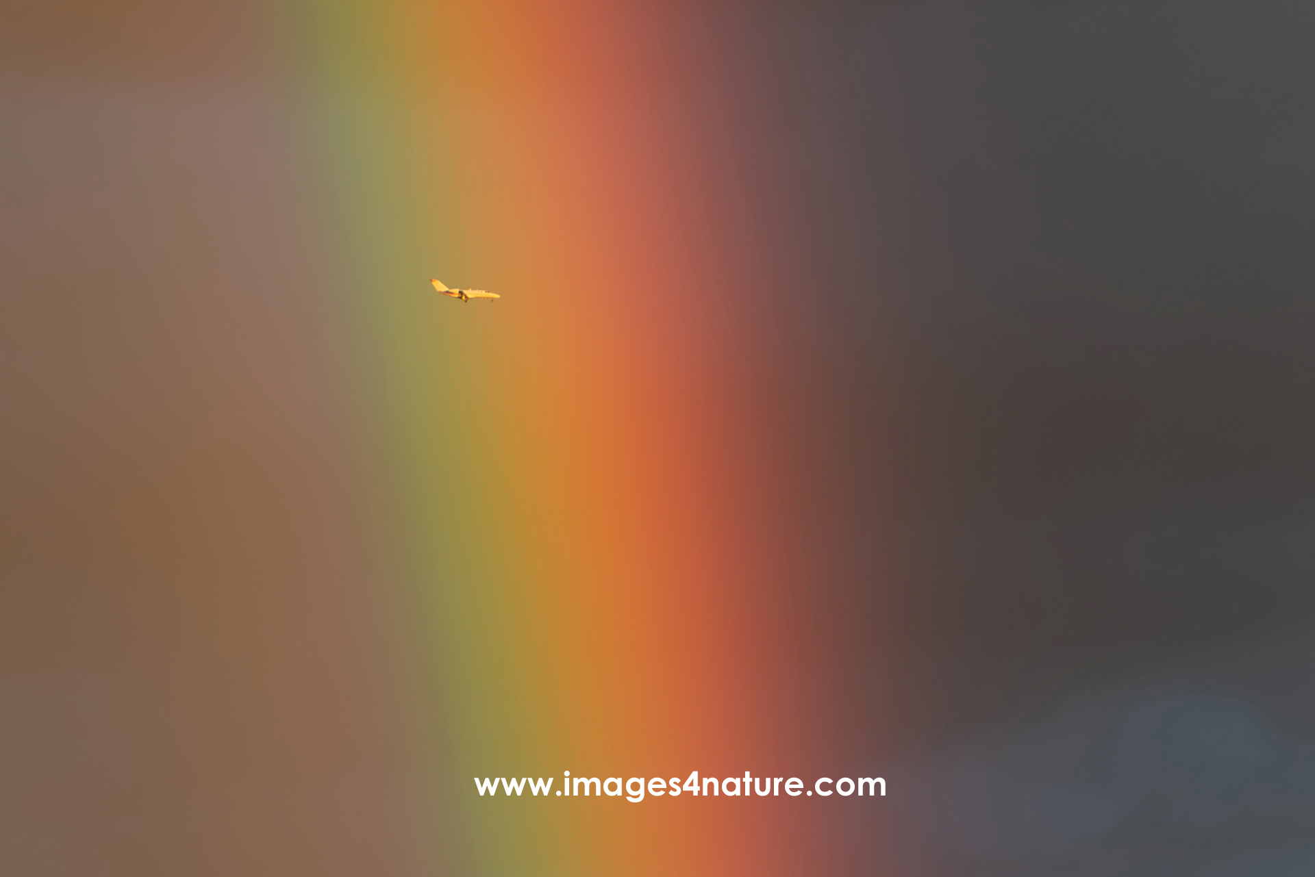 Closeup on a rainbow with a small jet plane flying though it