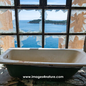 White bathtub in front of broken window of an abandoned hotel