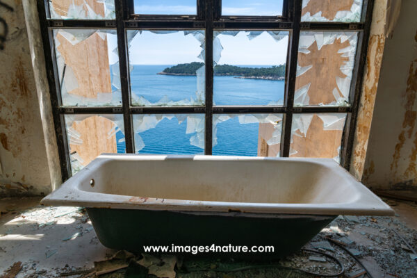 White bathtub in front of broken window of an abandoned hotel