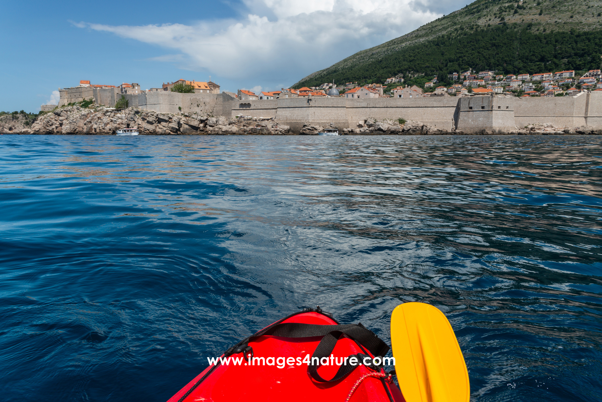 Red kayak and yellow paddle at sea, facing Dubrovnik city walls