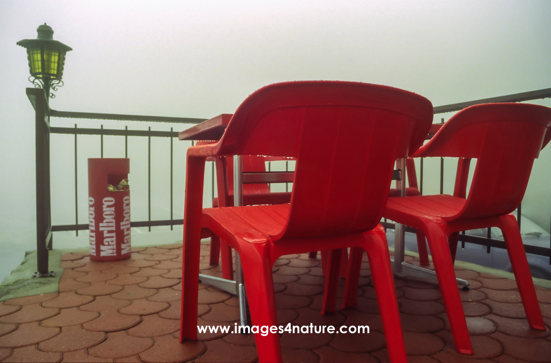 Red plastic chairs with table and dustbin on a foggy day