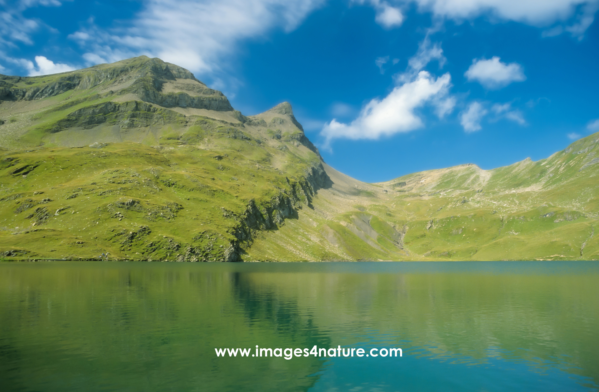 Summer alpine lake surrounded by mountains against blue sky