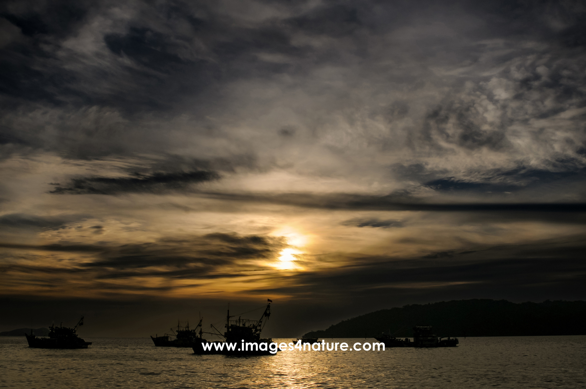 Silhouette of fishing boats at sunset against dark cloudy sky