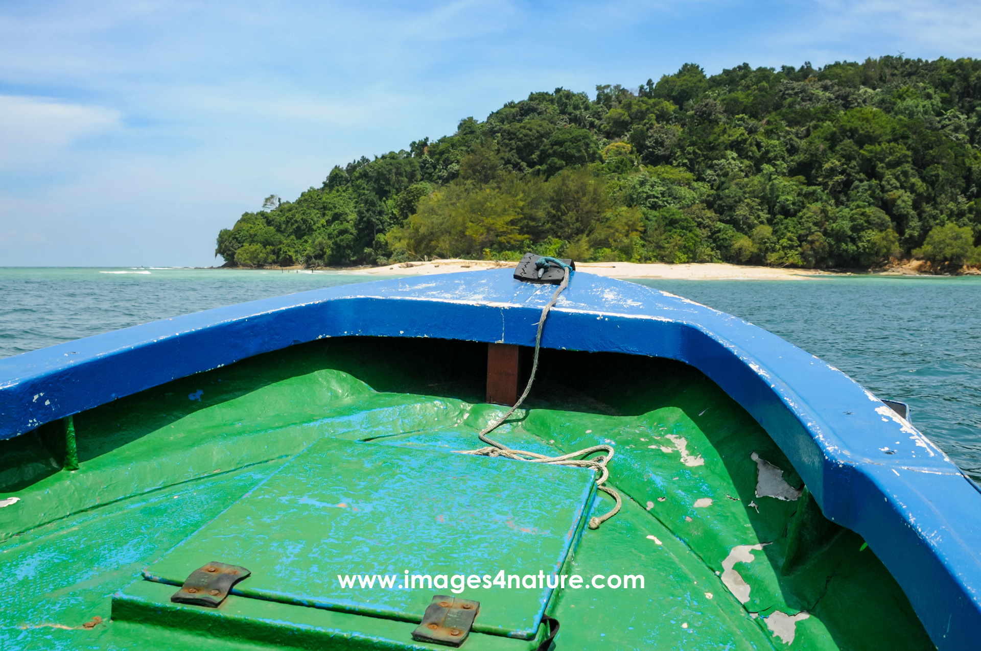 Small green and blue painted boat approach tropical island