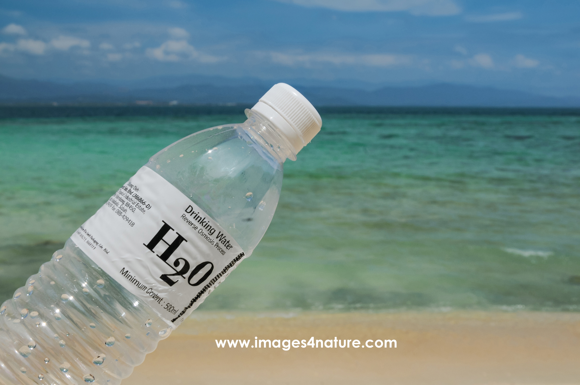 Empty plastic bottle against sandy beach, turquoise sea and sky