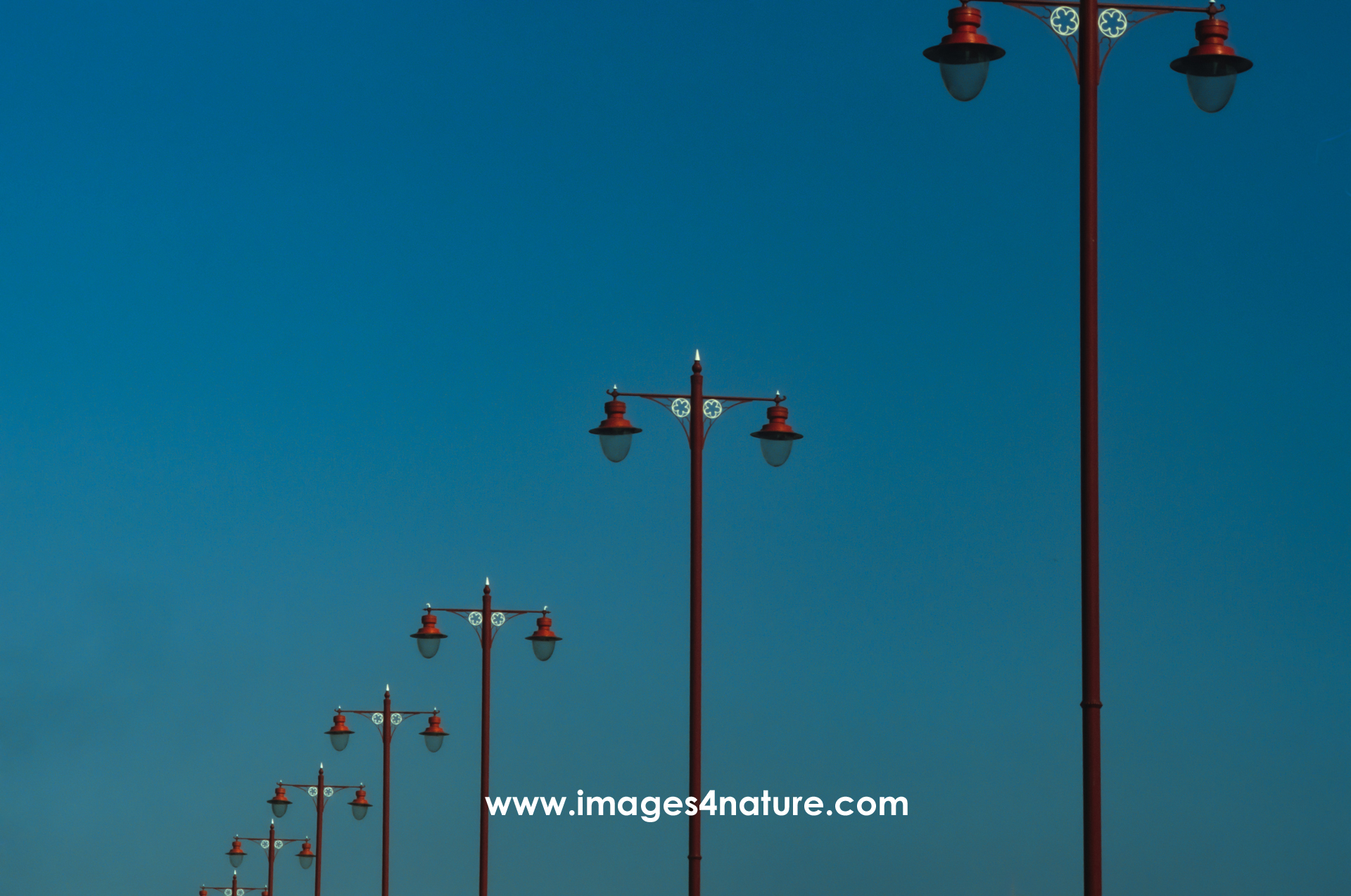 Six red double London street lamps against clear blue sky