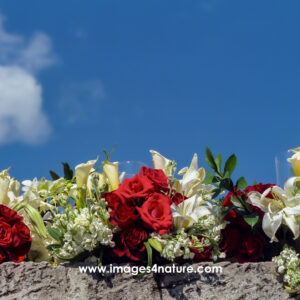 White and red flower bouquets on a stone wall against blue sky