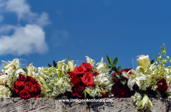 White and red flower bouquets on a stone wall against blue sky