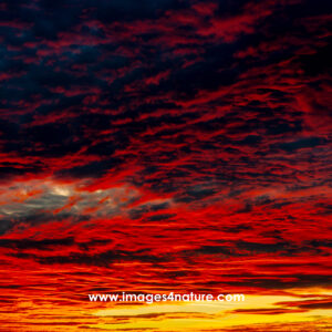 A small eye-shaped whole in an evening sky filled with red clouds and shades of yellow and orange