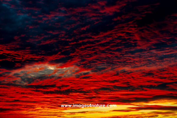 A small eye-shaped whole in an evening sky filled with red clouds and shades of yellow and orange