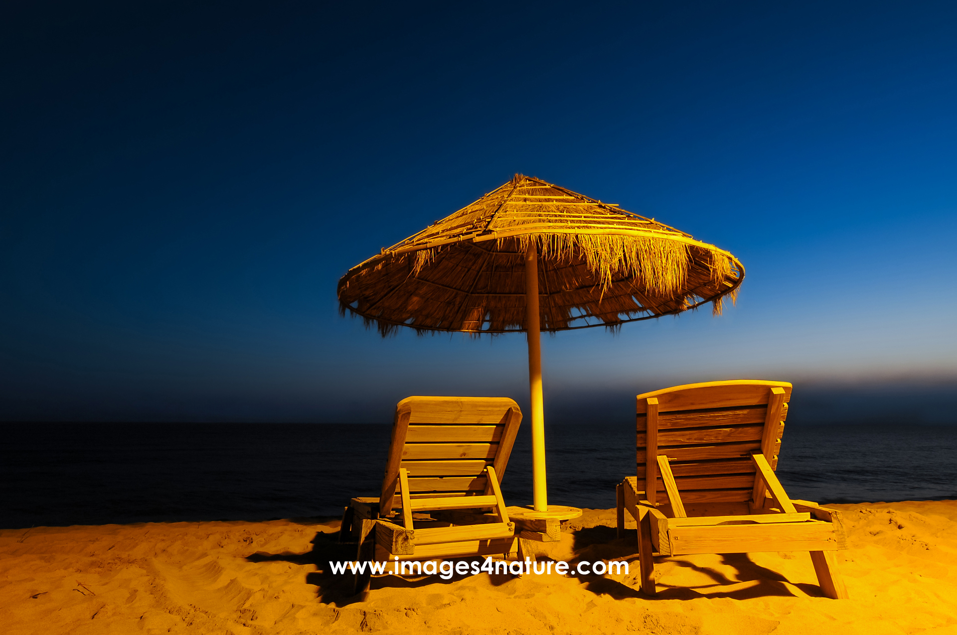 Sunshade and two lounge chairs on a sandy beach during blue hour