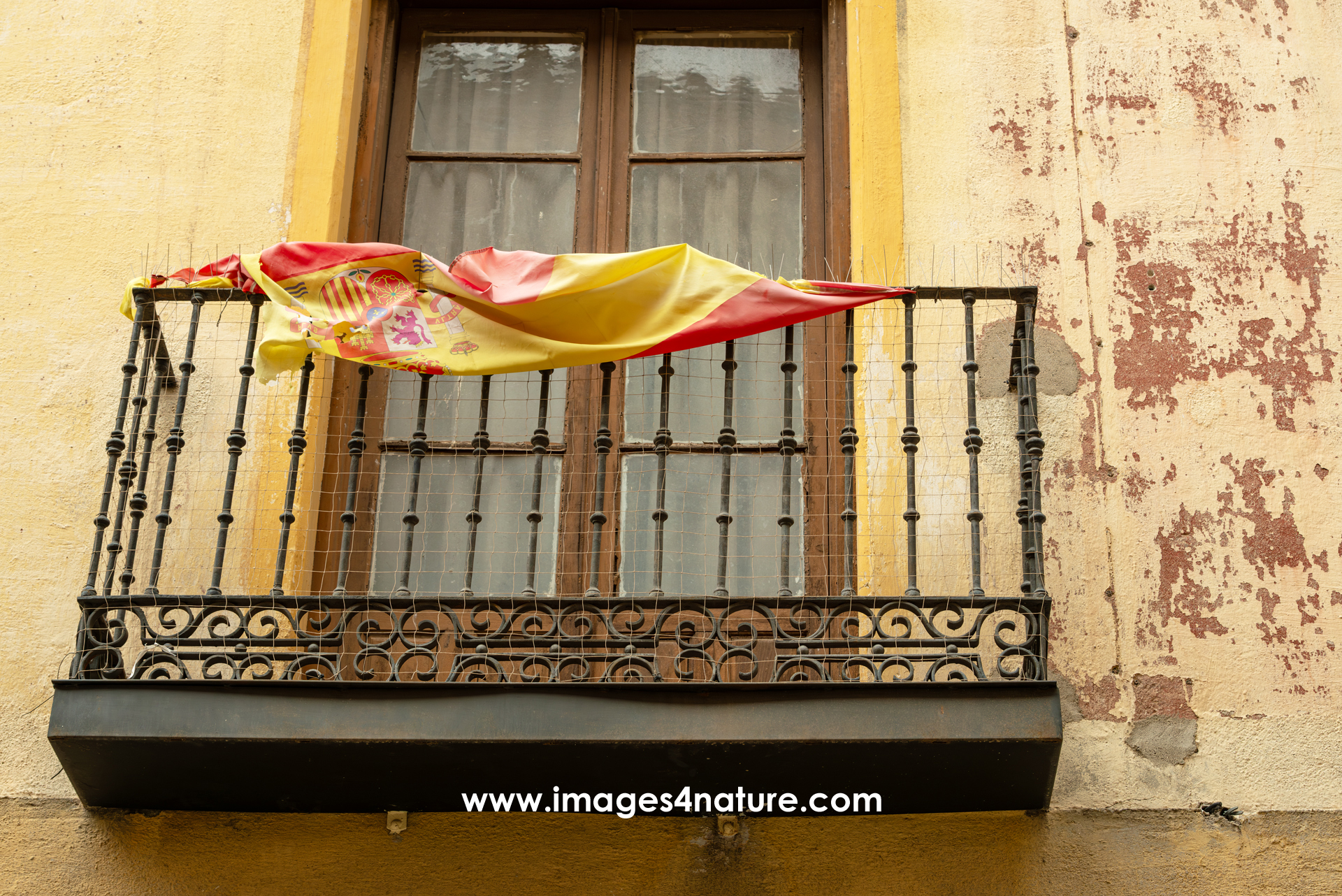 A balcony with a Spanish flag folded on top of the metal railing