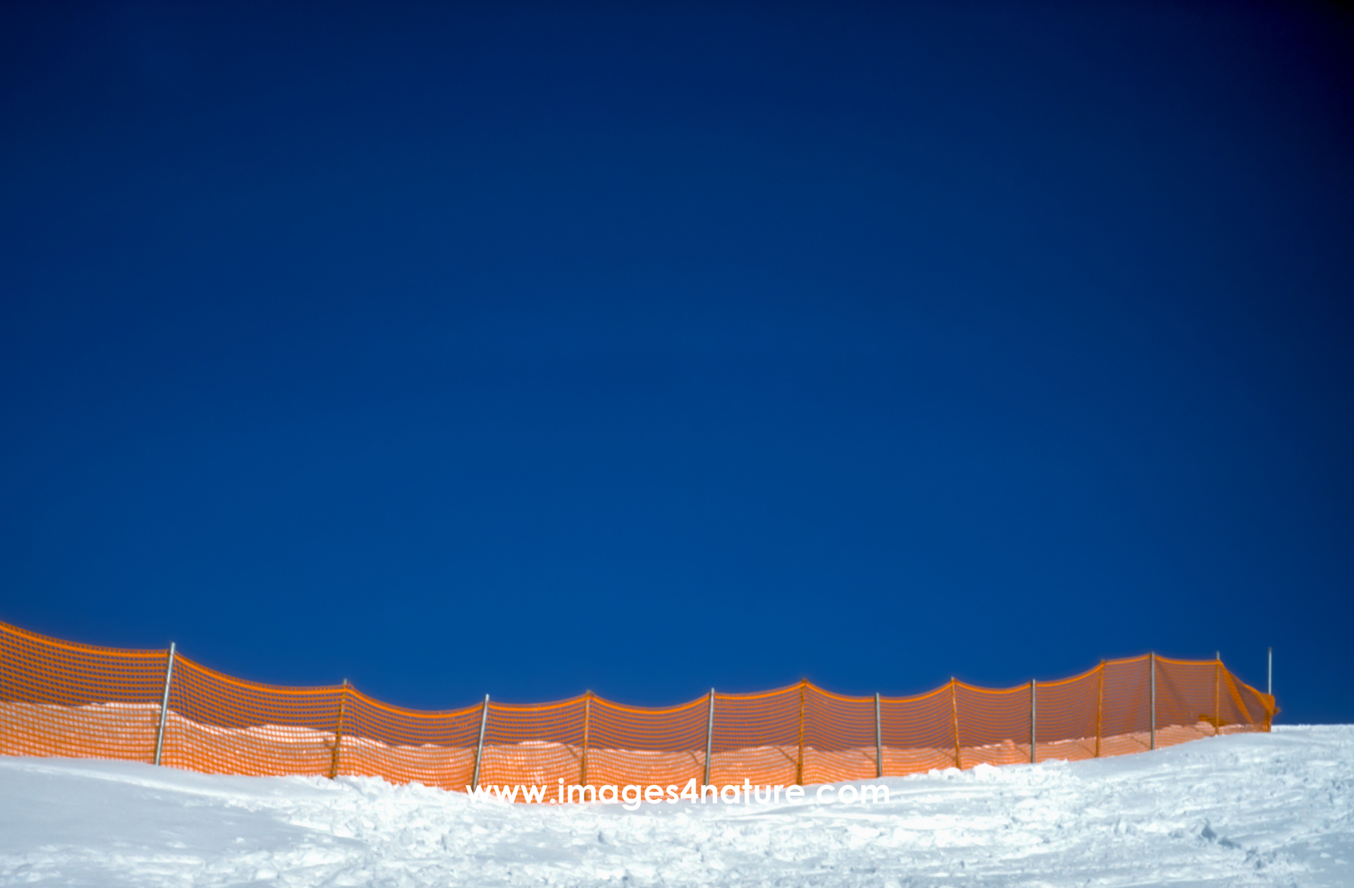 Orange plastic fence in the snow against dark blue sky
