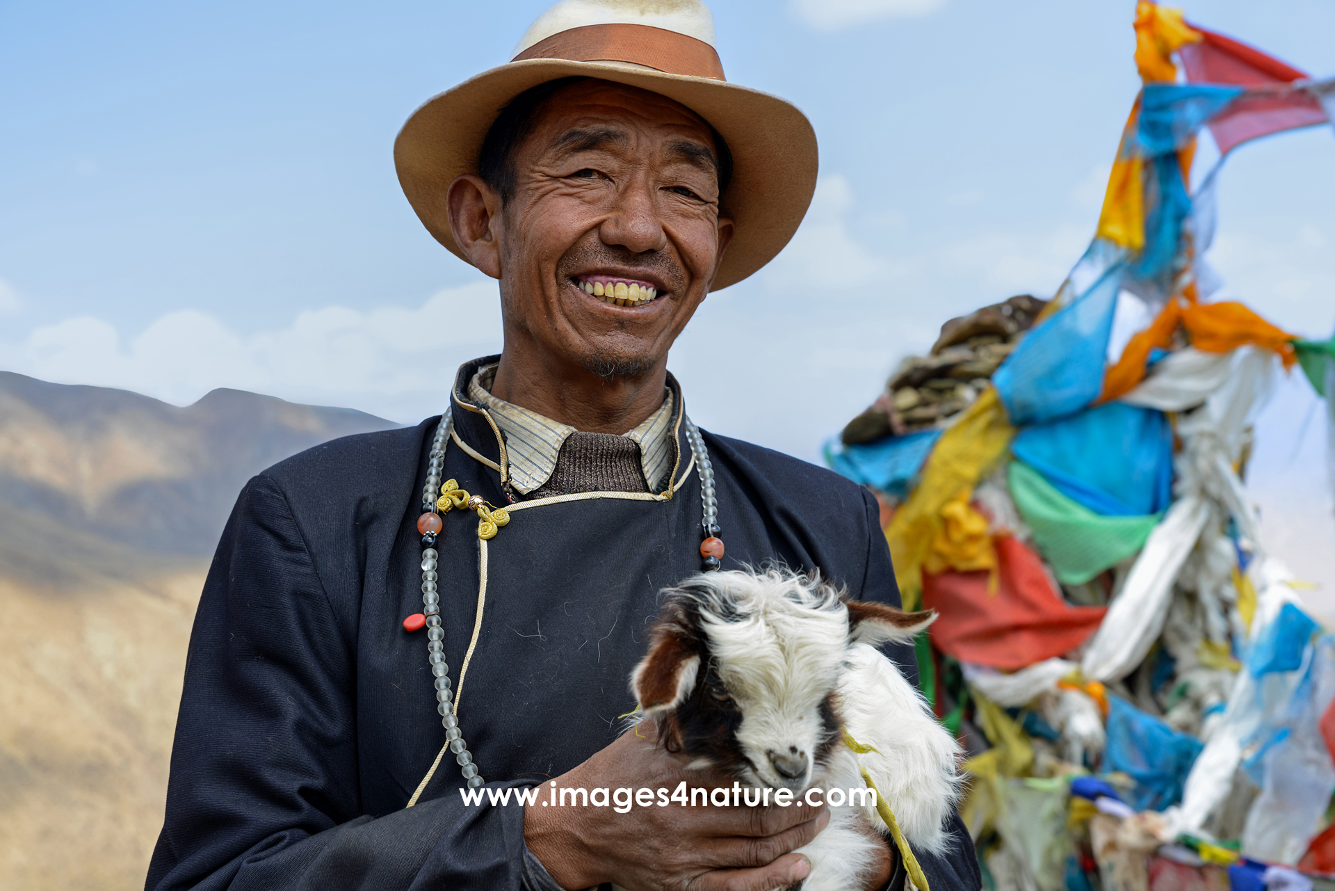 Portrait of smiling Tibetan farmer in traditional costume with little goat