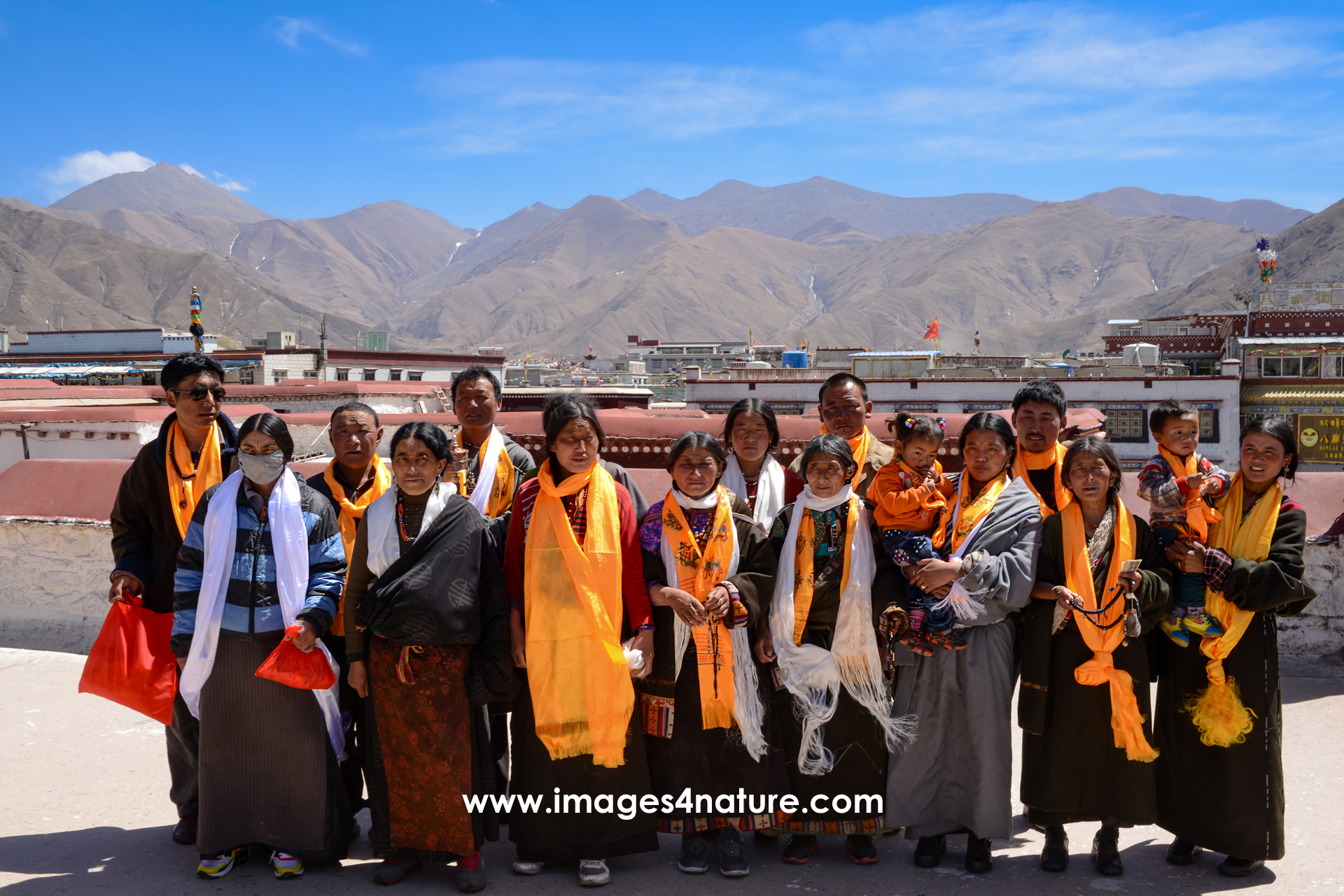 A group of sixteen Tibetan pilgrims on top of the Jokhang Temple against sky and mountain range