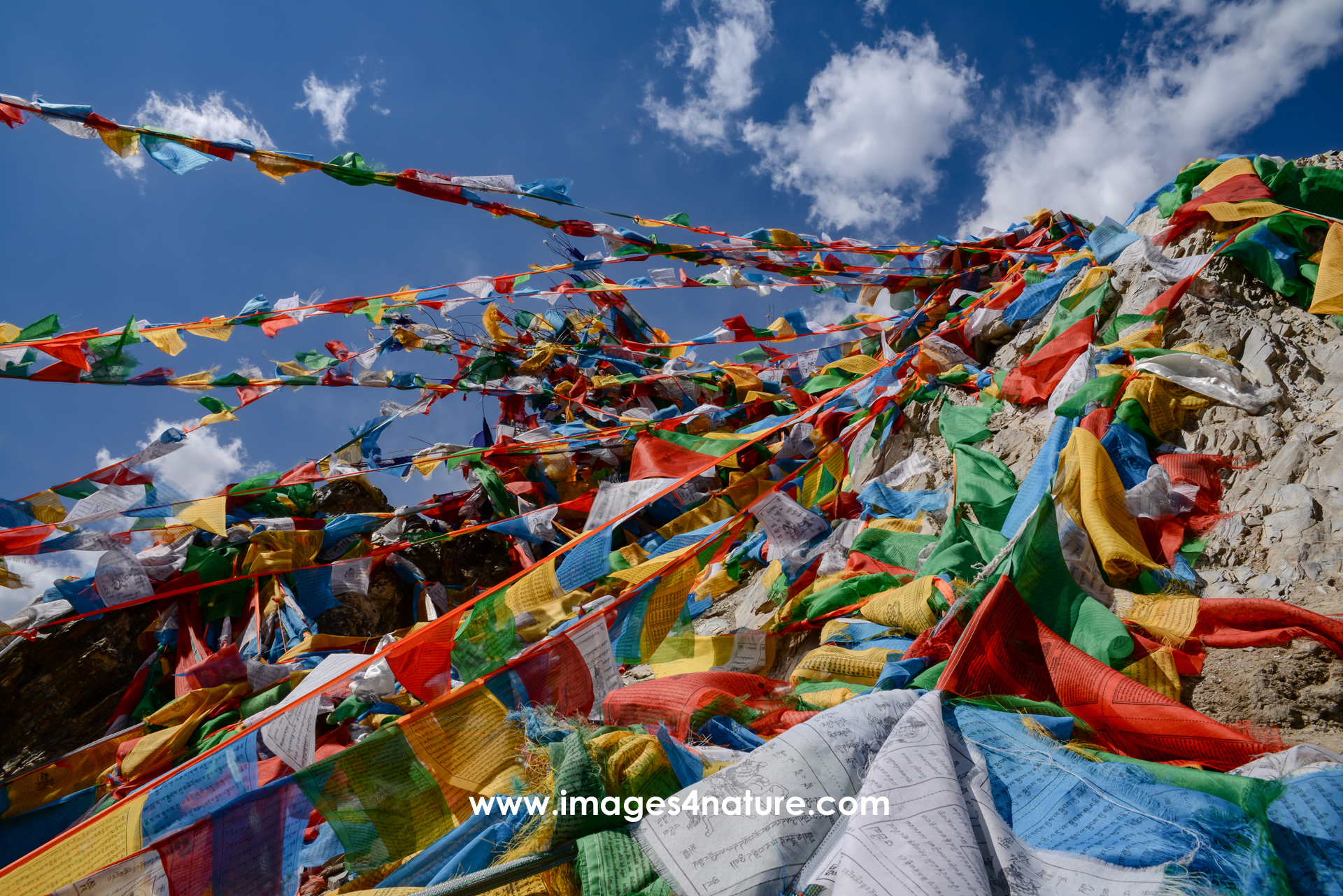 Low-angle view of many ropes with Tibetan prayer flags attached to a stony mountain peak