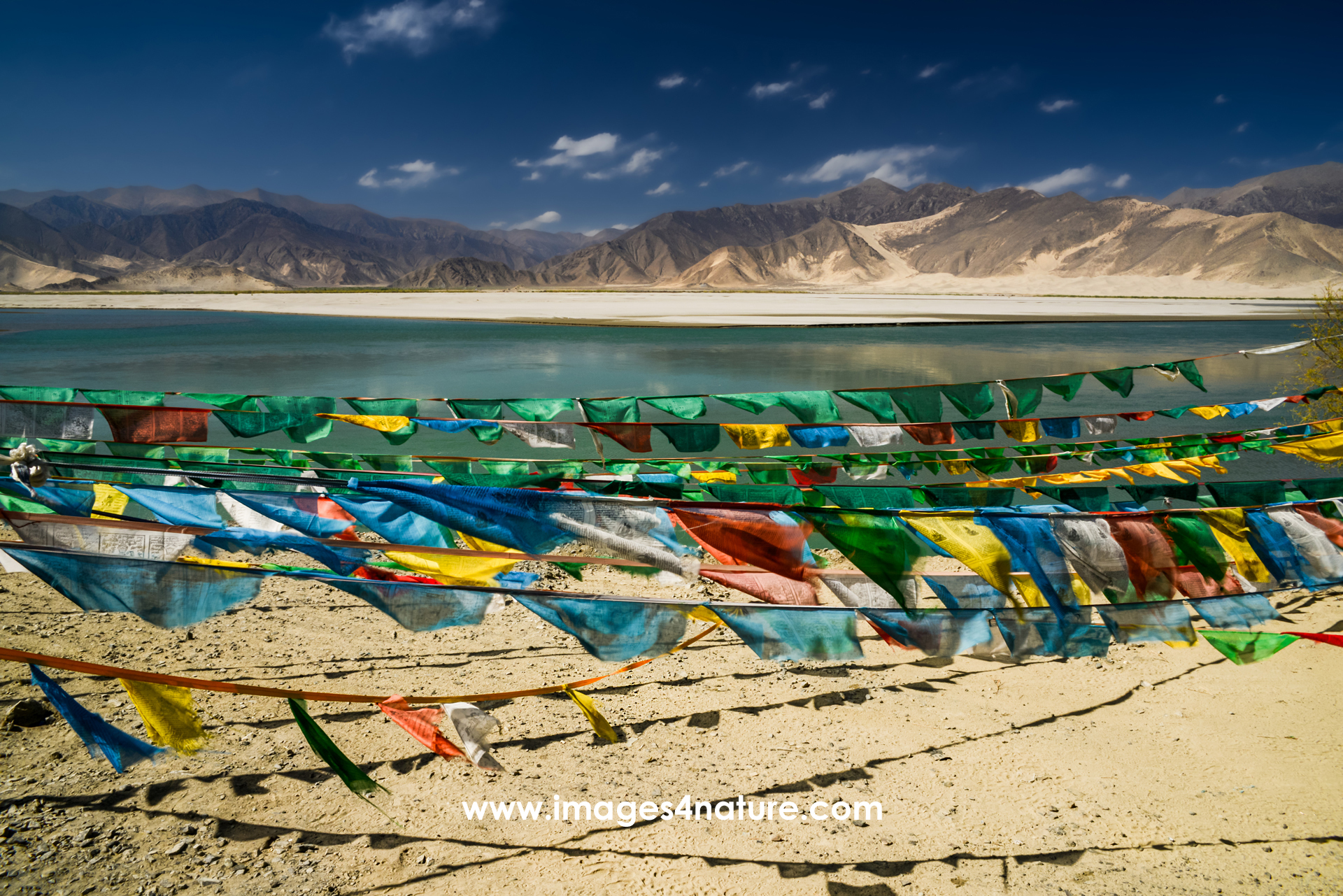 Highly color-saturated Tibetan prayer flags above the bank of the Yarlung Zangbo river flowing through Tibet mountain landscape