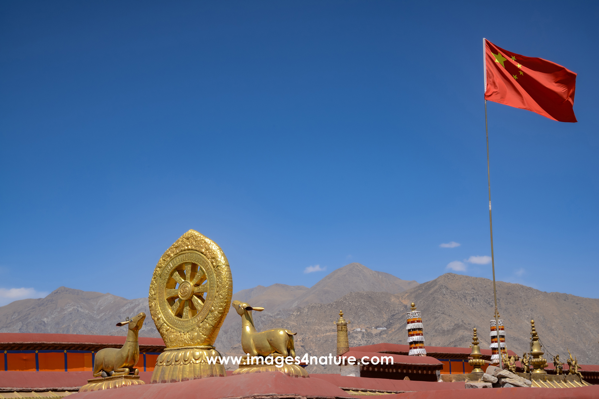 Golden dharma wheel and two lying deer on top of the Jokhang temple with mountain range in the background
