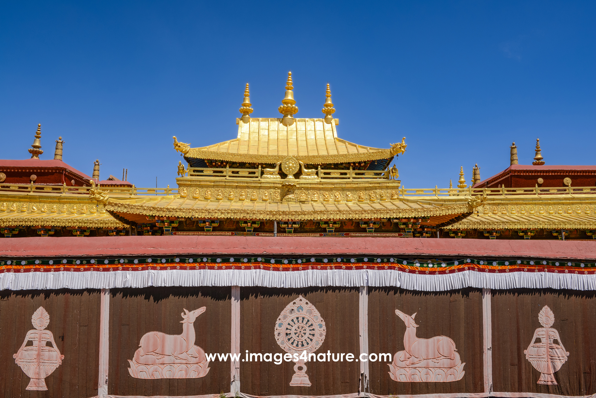 Close-up on wall with religious symbols and golden rooftop within the Jokhang Temple in Lhasa