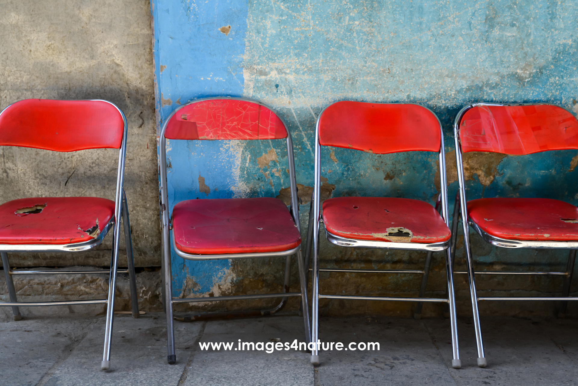 Line-up of four metal chairs with red seats and backs in front of a weathered blue wall