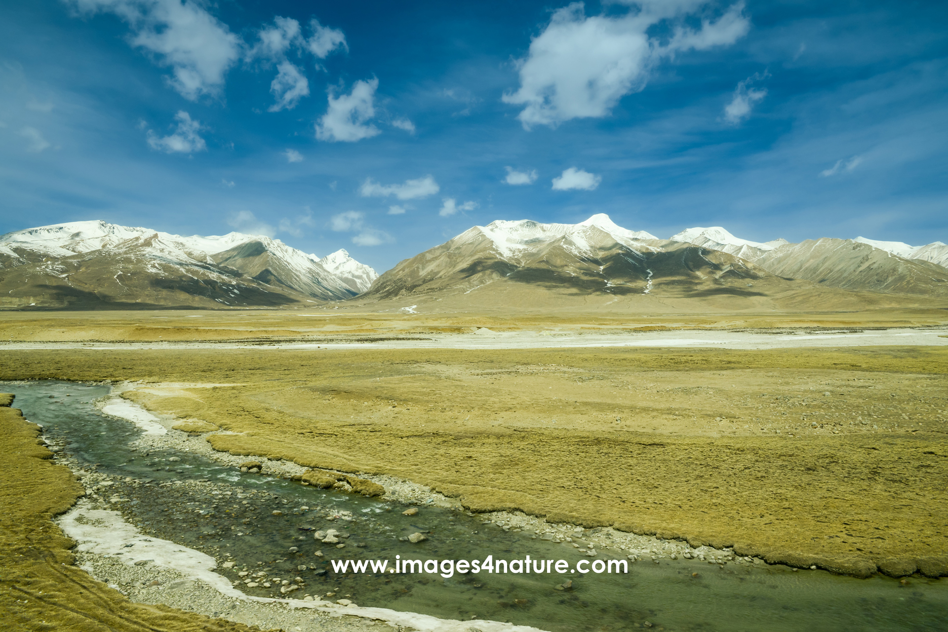 Qinghai-Tibet plateau landscape in winter with snow-covered mountain peaks and stream flowing through grasslands