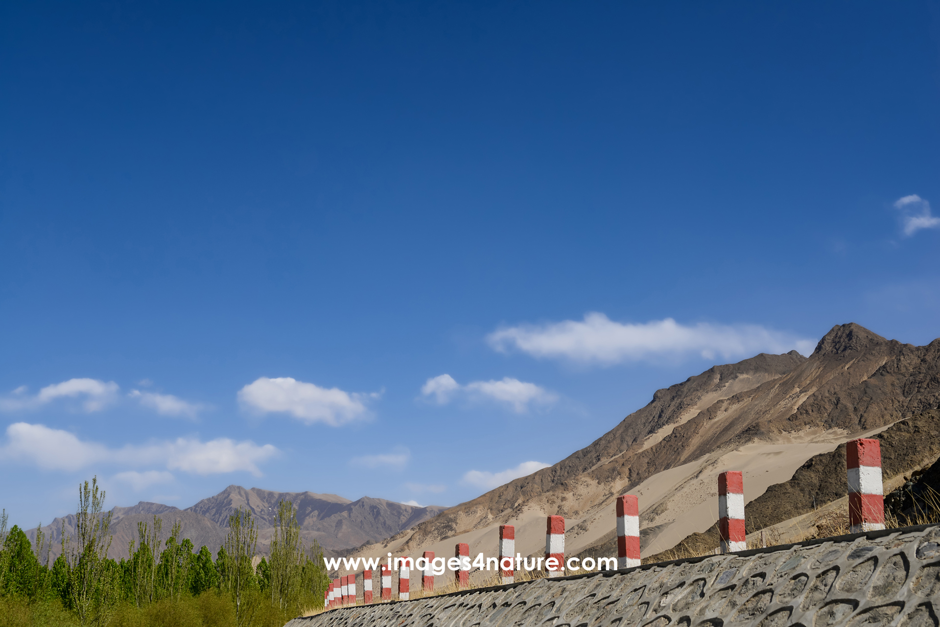 Low-angle view of white and red painted road guiding posts against mountains and blue sky