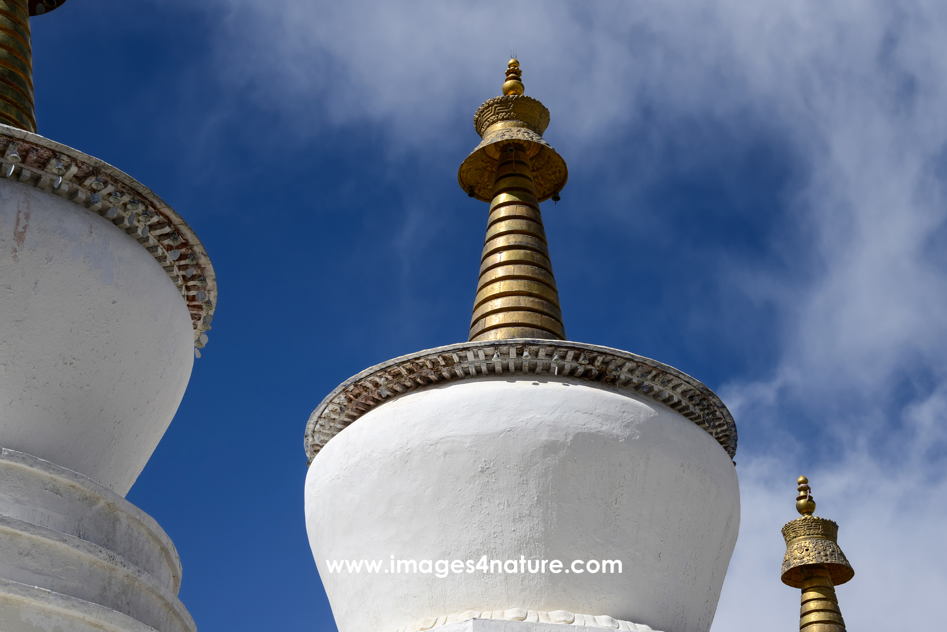 Low-angle view of white Tibetan stupas with golden top against blue sky