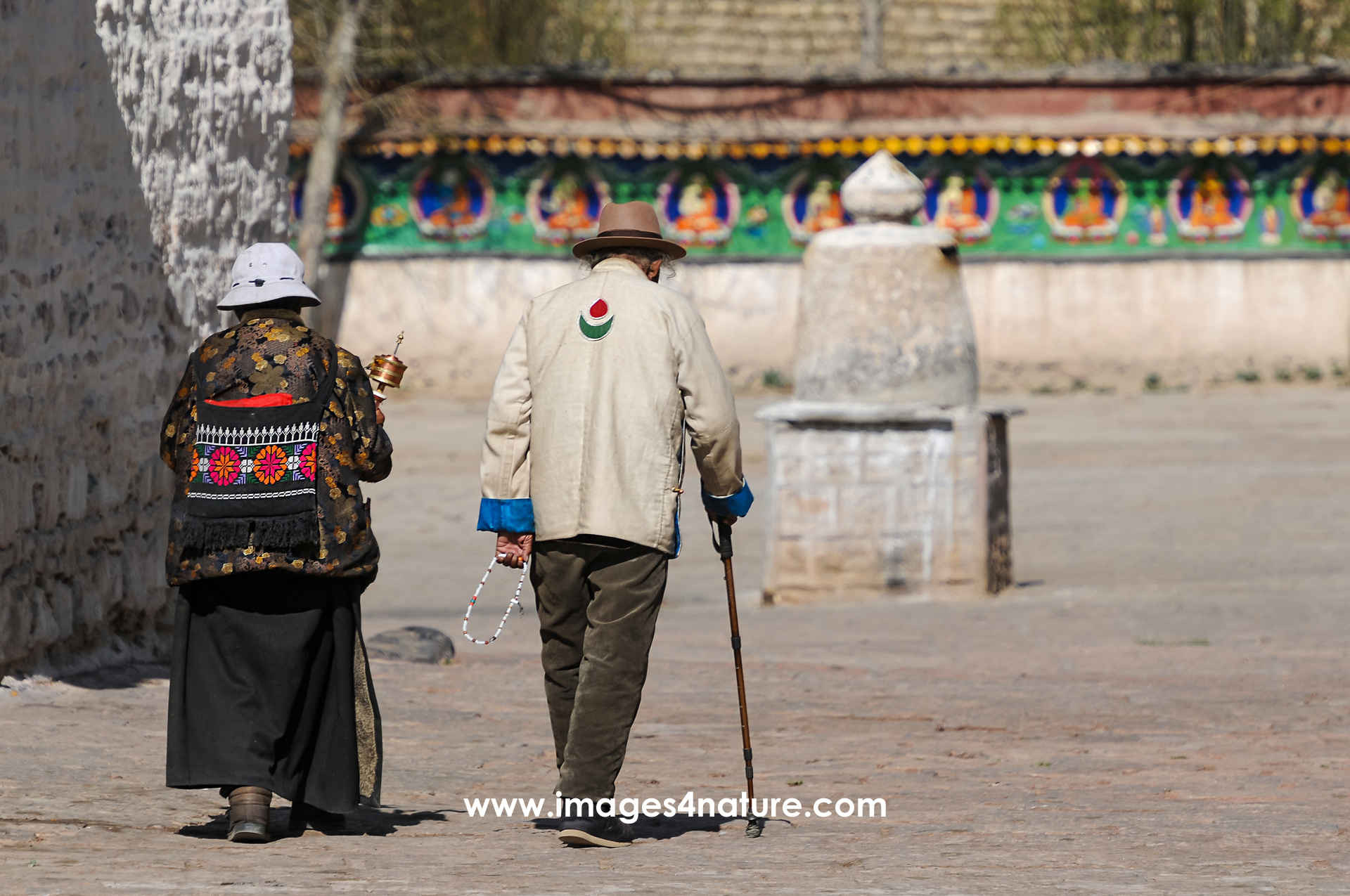 Rear view of an elderly couple in traditional clothes with prayer mill and walking stick