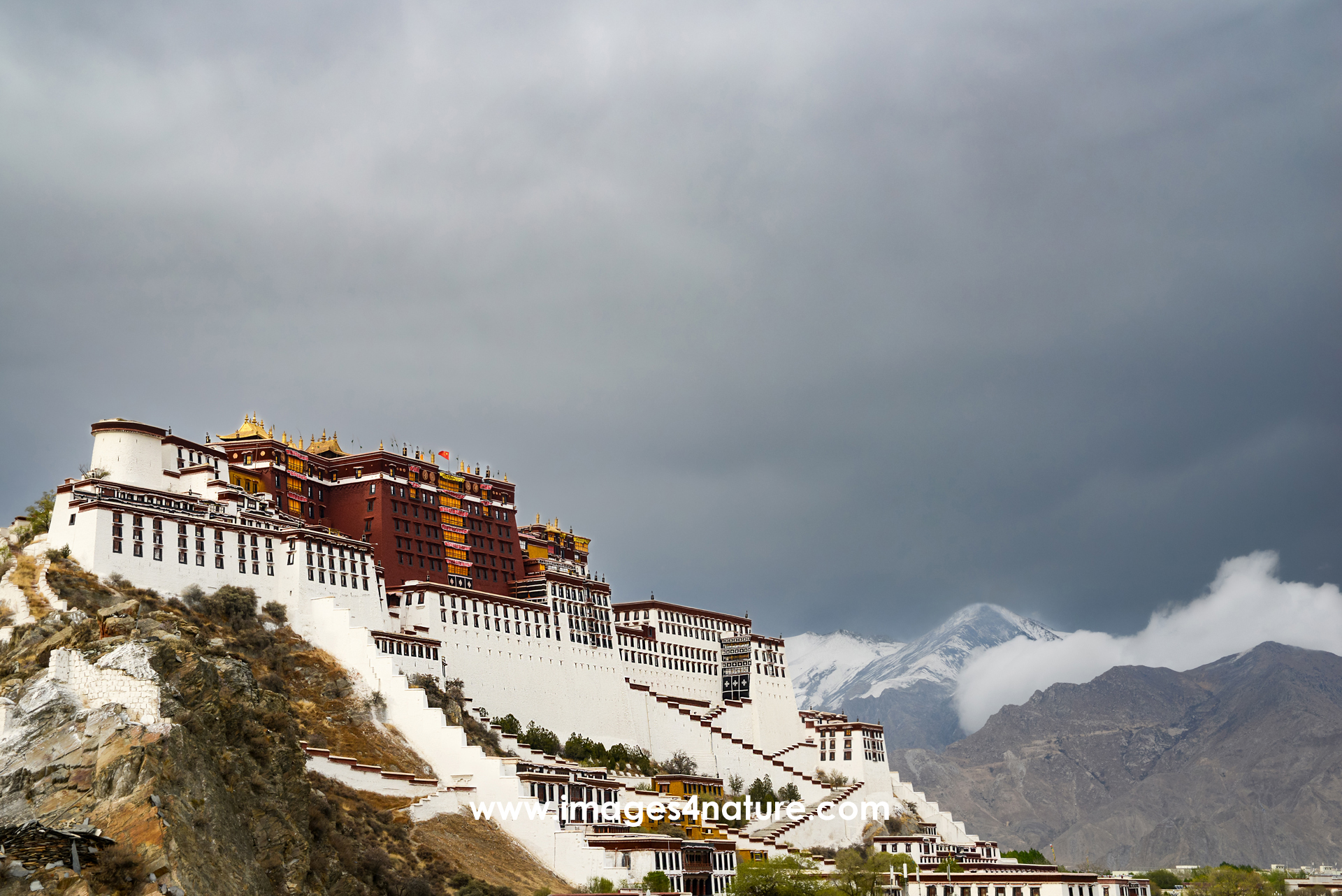 Diagonal scenic view of Lhasa's Potala Palace against cloudy snow-capped mountain peaks
