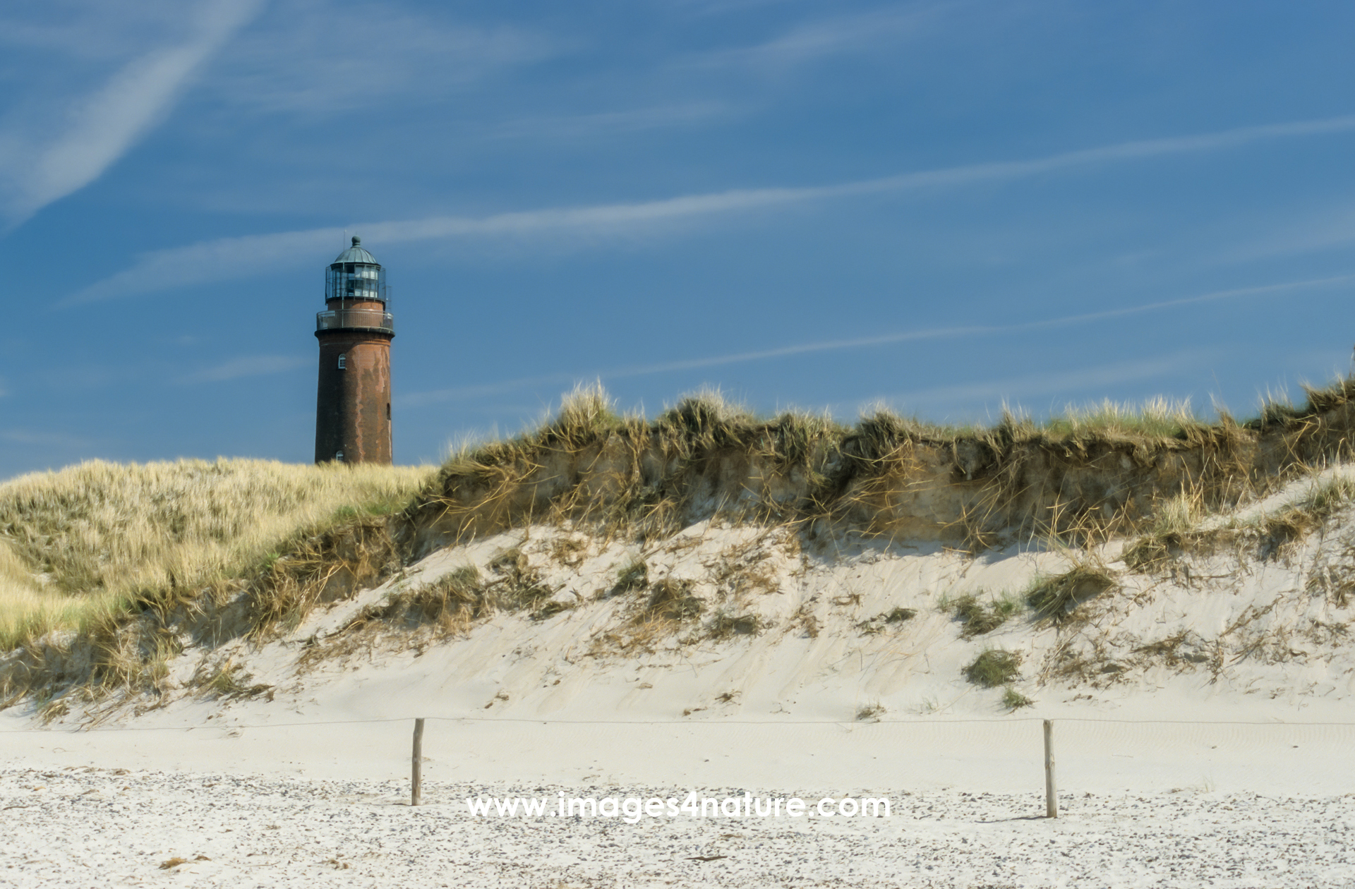 Grass covered sanddunes with red lighthouse on the left