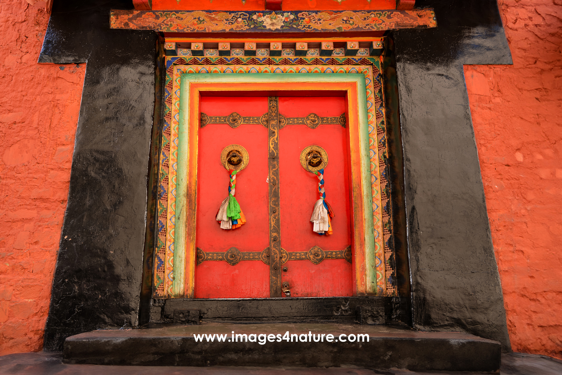 Orange wall with a massive black portal hosting a nicely decorated red wooden door