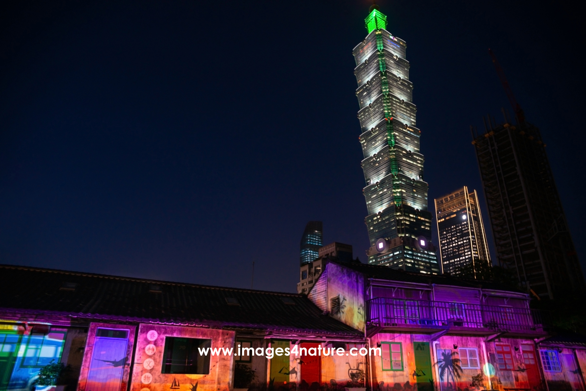 Horizontal late blue hour shot of Taipei 101 behind ancient buildings nicely illuminated by a colorful lightshow